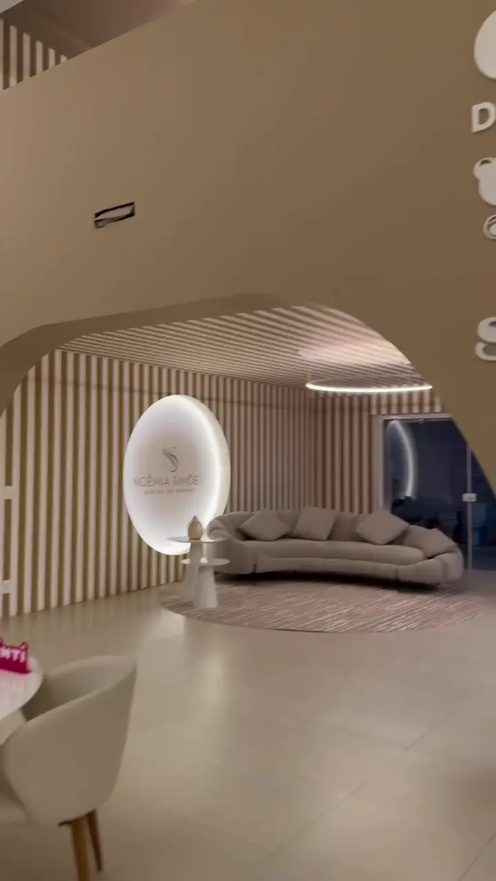 Lounge com sofá curvo, ripas no teto e o logo iluminado