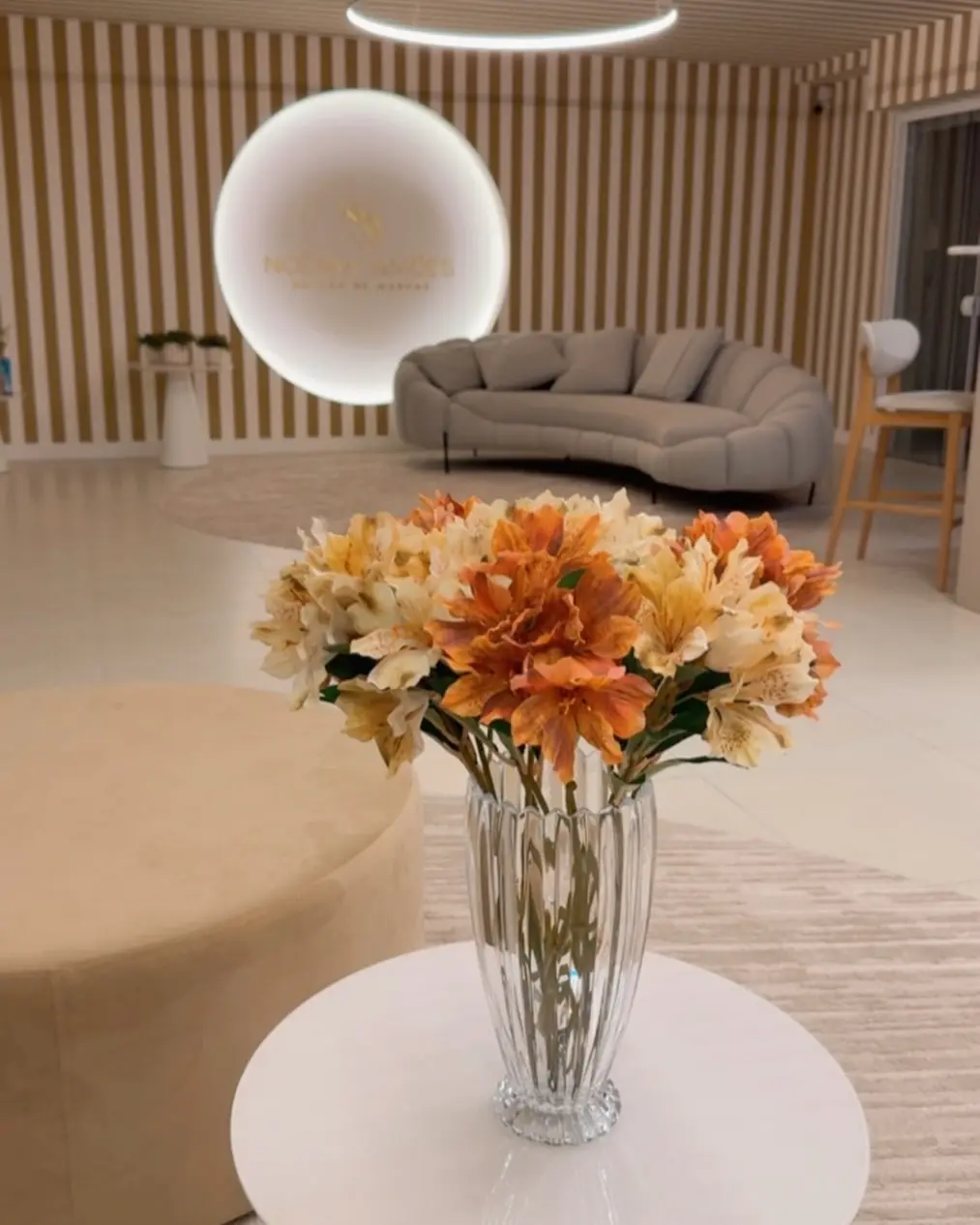 Mesa com vaso de flores laranja e o sofá do lounge ao fundo